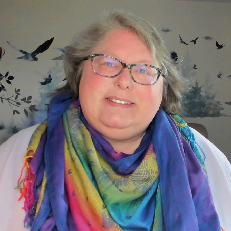 woman with blonde hair, shortish, glasses, wearing a rainbow scarf around her neck
